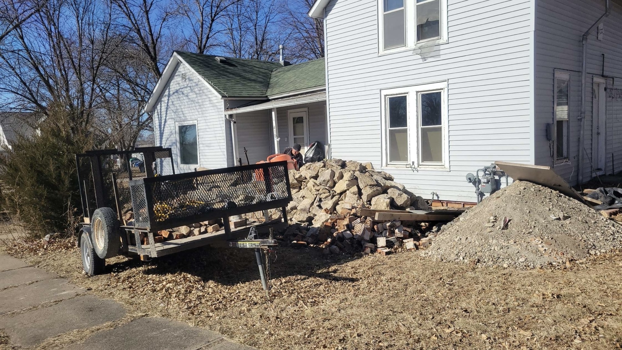 GrindStone Cleanup — Post-construction debris removal in action. Trailer loaded at job site with concrete, brick, and rubble being hauled away.